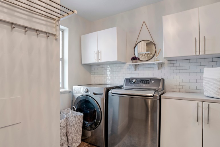 A modern laundry room with stainless steel washer and dryer, white cabinets, white tile backsplash, and laundry baskets.